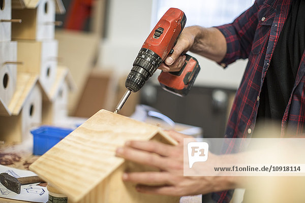 Man working with electric drill on birdhouse in workshop