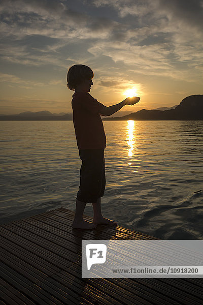 Junge hält bei Sonnenuntergang die Hände gegen die Sonne.