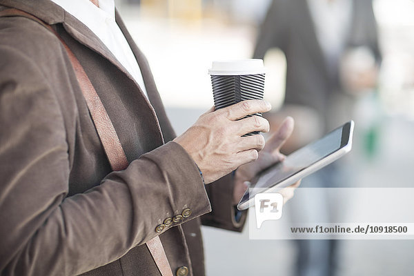 Mann mit digitalem Tablett und Kaffee für unterwegs