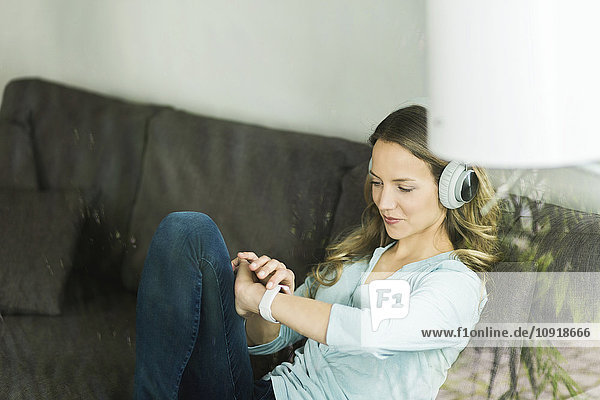 Frau zu Hause auf der Couch mit Kopfhörer und Blick auf smartwatch