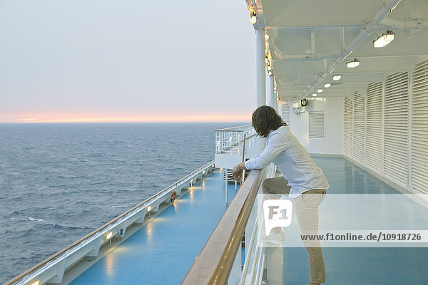 Junger Mann  der auf dem Schiff steht und den Sonnenuntergang beobachtet.