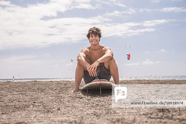 Porträt eines lächelnden jungen Mannes auf dem Surfbrett am Strand