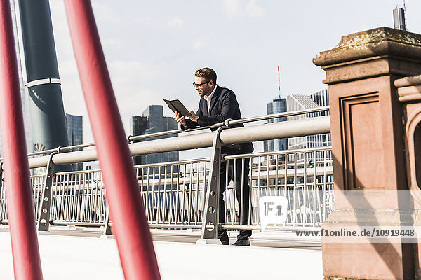 Junger Geschäftsmann mit digitalem Tablett auf der Brücke stehend