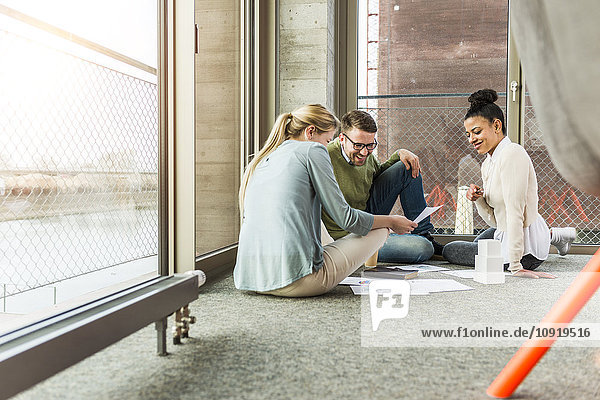 Three colleagues in office sitting on floor working together