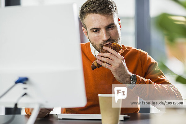 Junger Mann beim Snack am Schreibtisch im Büro
