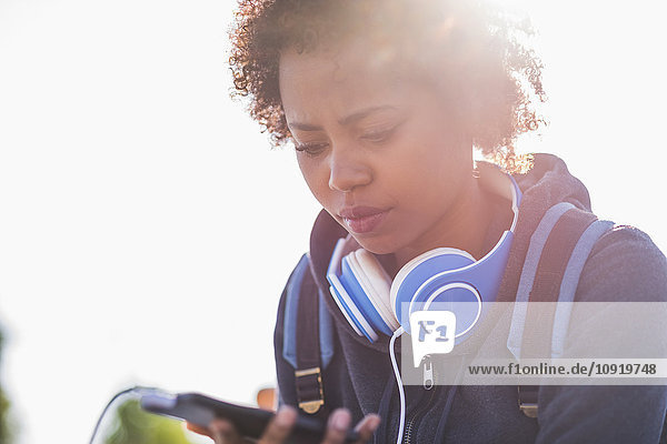 Young woman wearing headphones looking at cell phone outdoors