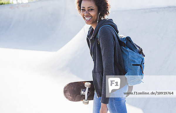 Happy young woman with skateboard listening to music