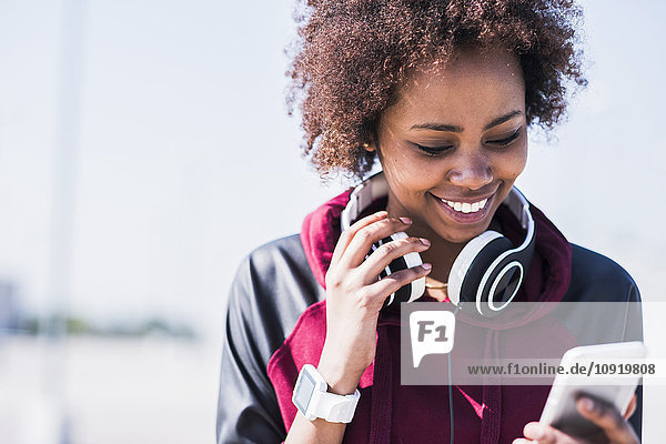 Smiling young woman wearing headphones looking at cell phone outdoors