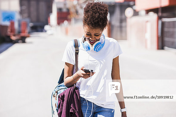 Smiling young woman wearing headphones looking at cell phone outdoors