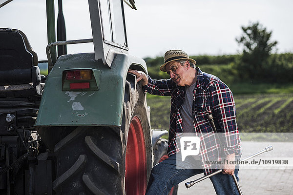 Farmer holding tool examining tractor tyre