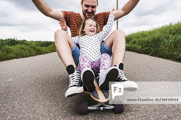 Tochter und Vater sitzen auf dem Skateboard