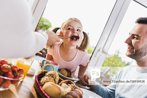 Girl with family licking spoon at breakfast table