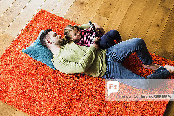 Vater und Tochter liegen auf einem Teppich auf dem Boden mit Hilfe eines digitalen Tabletts.