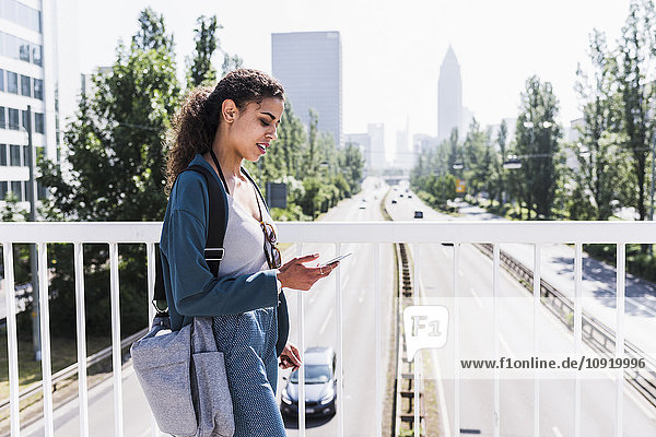 Junge Frau auf der Brücke beim Blick aufs Handy