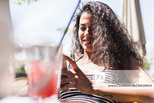 Lächelnde junge Frau beim Blick auf das Handy im Freien