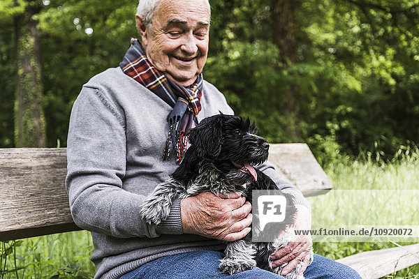 Lächelnder älterer Mann sitzt mit seinem Hund auf einer Bank in der Natur.