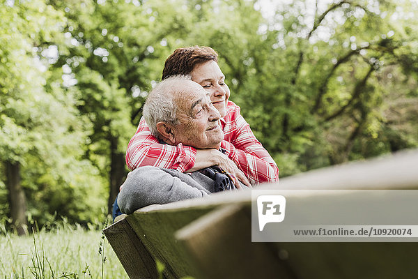 Glückliche Frau umarmt ihren alten Vater auf einer Bank in der Natur.
