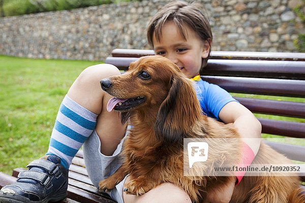 Kleiner Junge mit Hund auf einer Bank sitzend