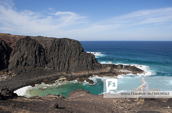 Spanien  Kanarische Inseln  Fuerteventura  Punta del mal Rayo  Agua Cabras  Wanderer sitzend auf Stein