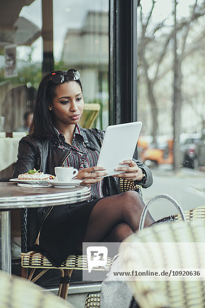 Porträt einer jungen Frau,  die in einem Cafe sitzt und ein digitales Tablett benutzt.