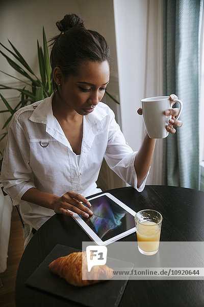 Junge Frau mit digitalem Tablett am Frühstückstisch