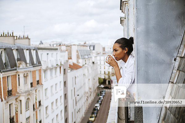 Frankreich  Paris  junge Frau mit Tasse Kaffee aus dem Fenster gelehnt