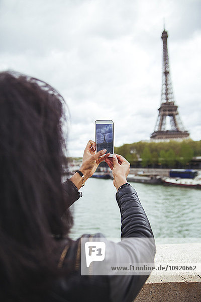 Frankreich  Paris  Junge Frau beim Fotografieren des Eiffelturms mit Smartphone