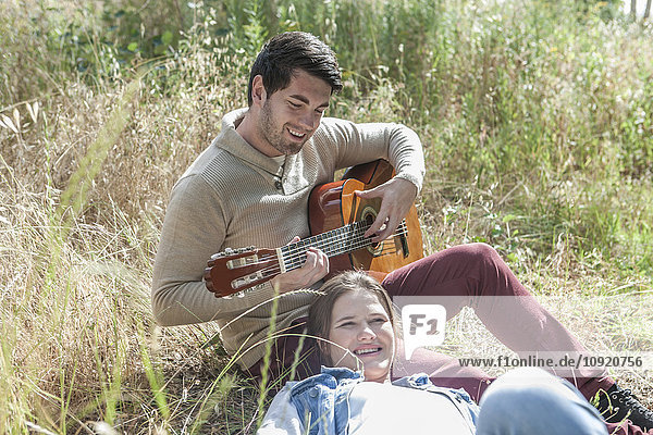 Junger Mann spielt Gitarre für seine Freundin im Feld