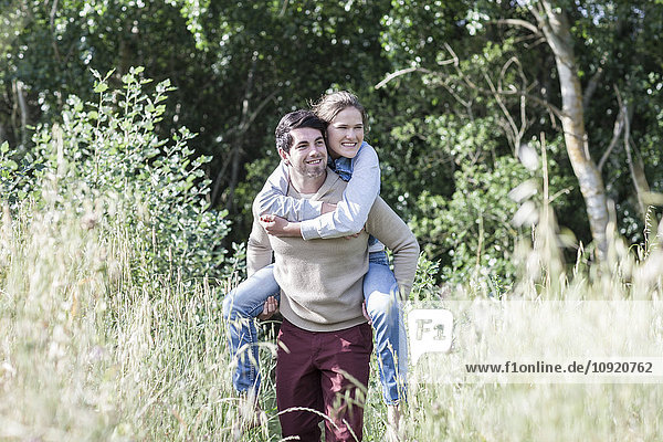 Young man carrying his girfriend piggyback in the nature