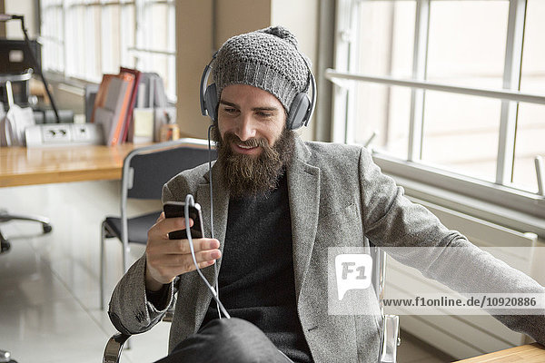Portrait of young businessman wearing beany hat using smart phone