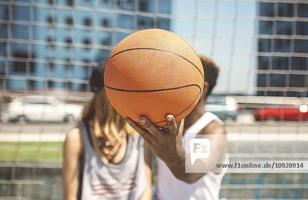 Junges Paar versteckt Gesichter hinter Basketball