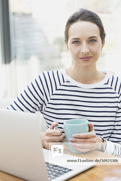 Portrait confident woman drinking coffee at laptop