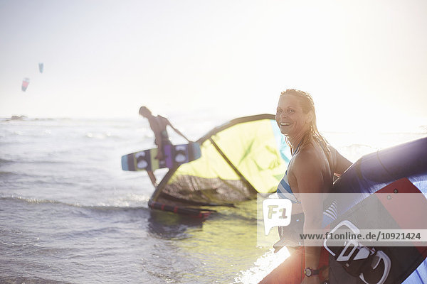 Portrait lächelnde Frau mit Kiteboardausrüstung in der Meeresbrandung
