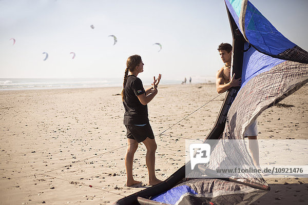 Frau unterrichtet Mann mit Kitesurfdrachen am sonnigen Strand