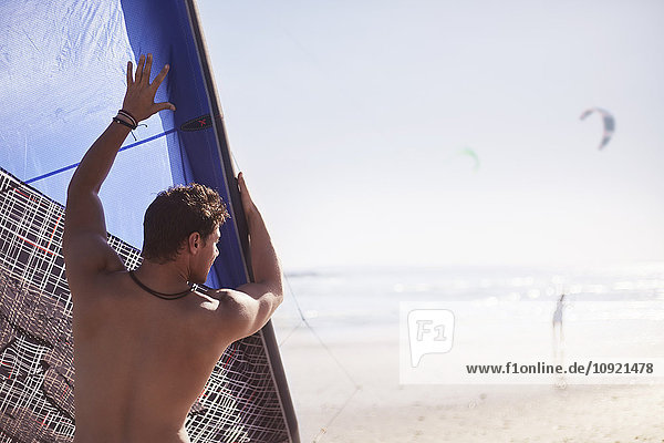 Man lifting kiteboarding kite on sunny beach