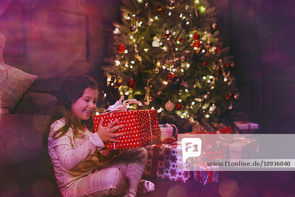 Aufgeregtes Mädchen mit Geschenk neben dem Weihnachtsbaum