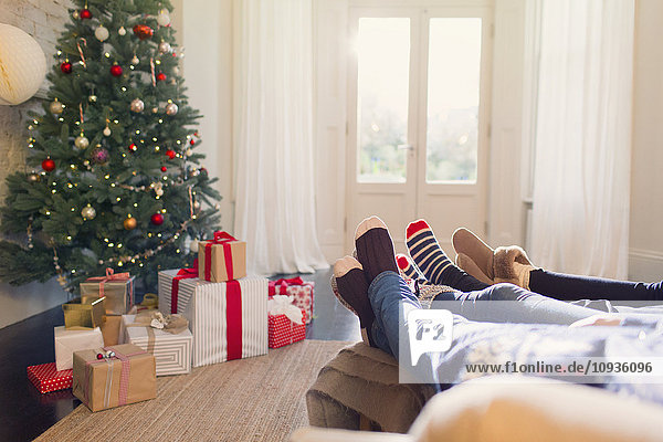 Entspannte Familie in Socken mit Füßen in der Nähe des Weihnachtsbaums