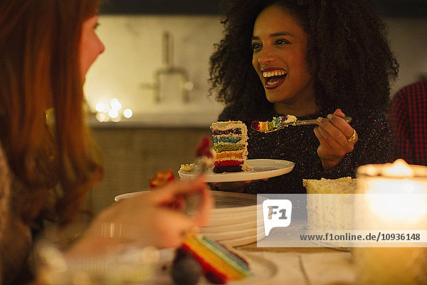 Lachende Freunde genießen Kuchen am Kerzenschein-Tisch