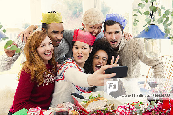 Friends wearing paper crowns taking selfie at Christmas dinner