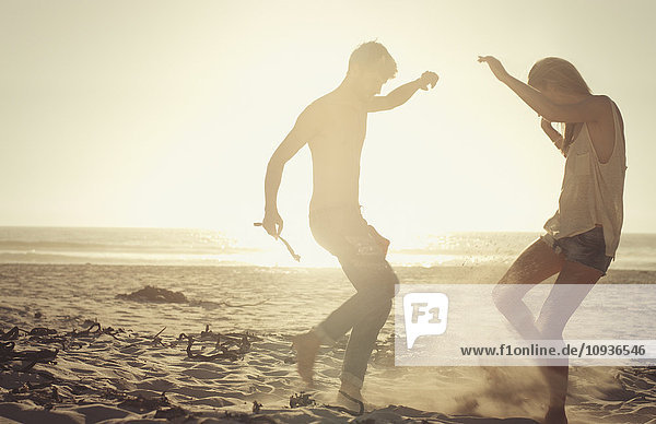 Verspieltes Paar tanzt am sonnigen Strand bei Sonnenuntergang