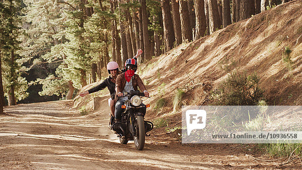 Übermütige junge Frau fährt Motorrad auf unbefestigtem Weg im Wald