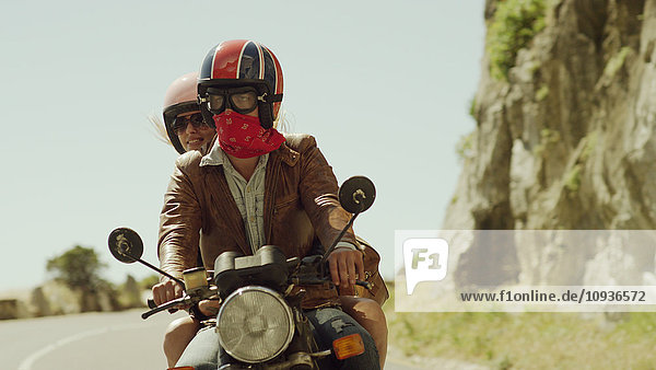 Junges Paar fährt Motorrad auf sonniger Straße