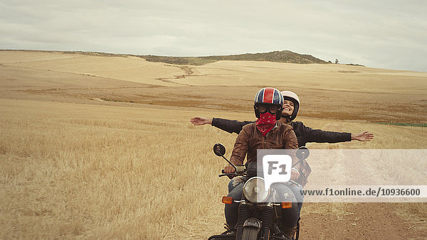 Exuberant young woman riding motorcycle in rural countryside