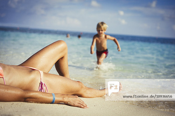 Sohn läuft auf Mutter zu  die sich am sonnigen tropischen Strand sonnt
