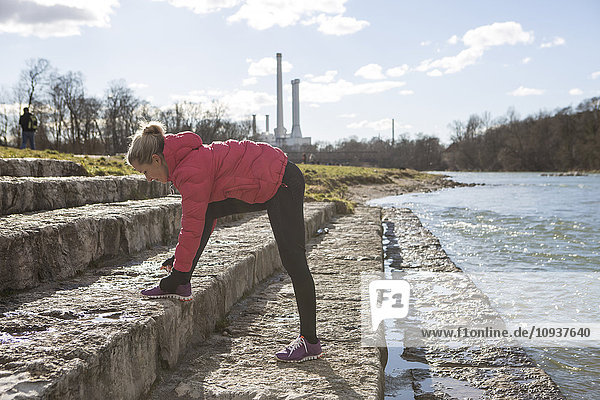 Blond woman tying sports shoe lace by the riverside