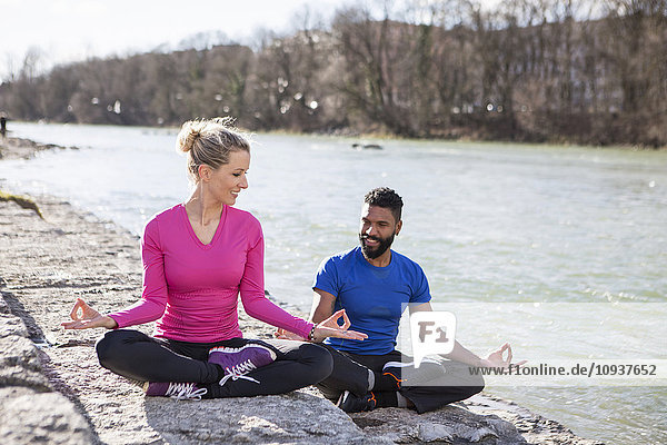 Young couple practicing yoga by the riverside