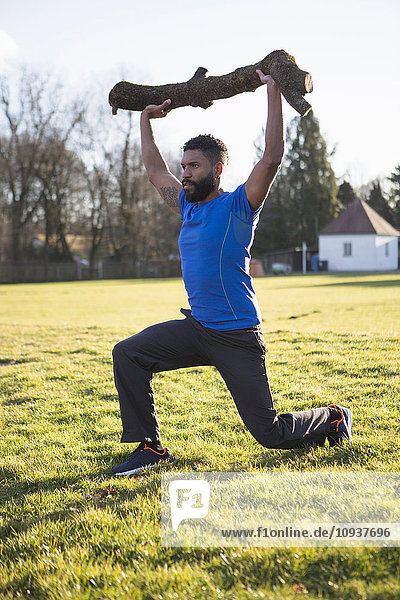 Young man doing squats with tree trunk on shoulder