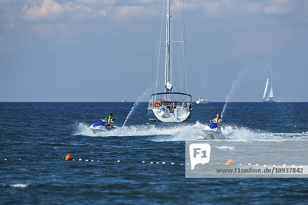 Jet boats racing at high speed next to sailboat