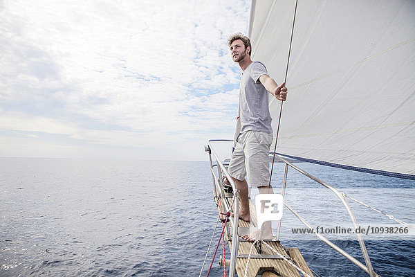 Man on bow of sailboat looking out over sea