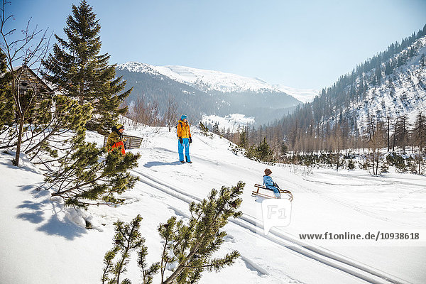 Boy sledding downhill with parents watching